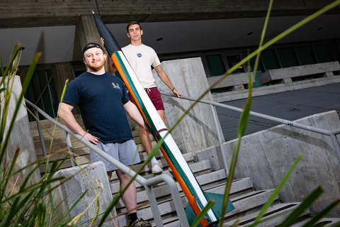Aerospace engineering students Tristan Peterson, left, president of Rocket ’Canes, and Matthew Burian, the club's project manager, display the Ibis 1 rocket, which now features a Hurricane orange-and-green paint scheme. 